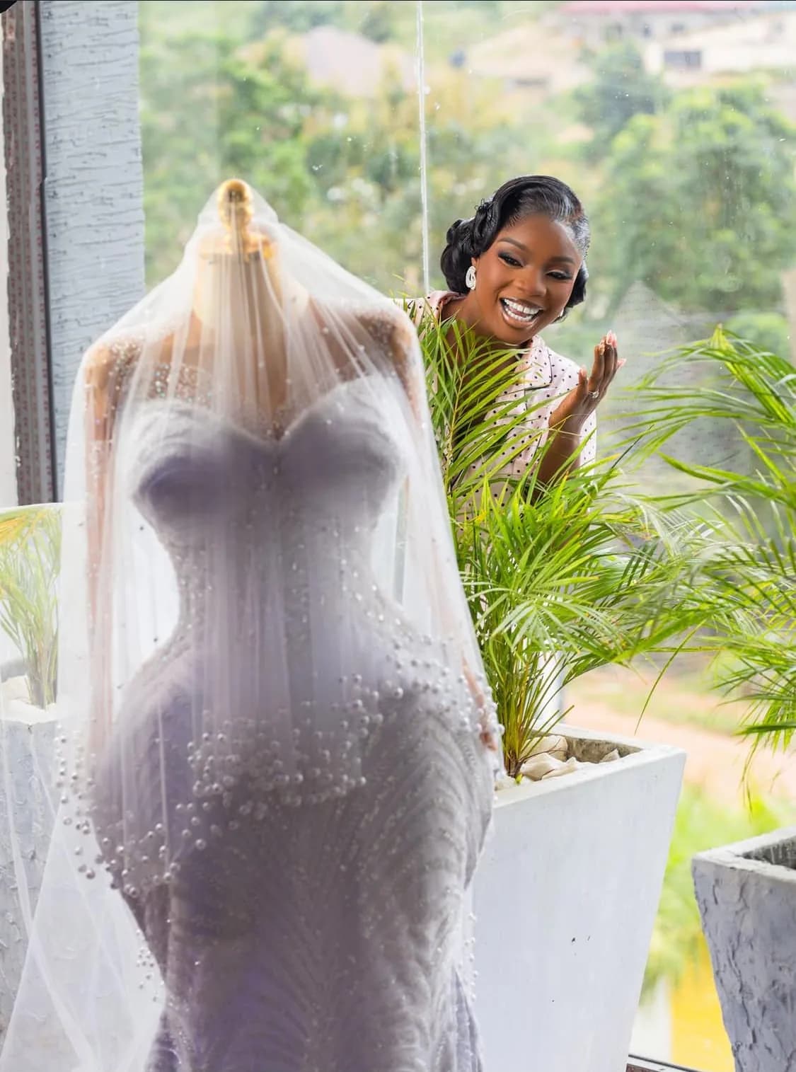 A beaded mauve mermaid gown displayed on a mannequin beneath a pearl-edged veil inside the Magmens Couture atelier, with a member of the couture team beside it.