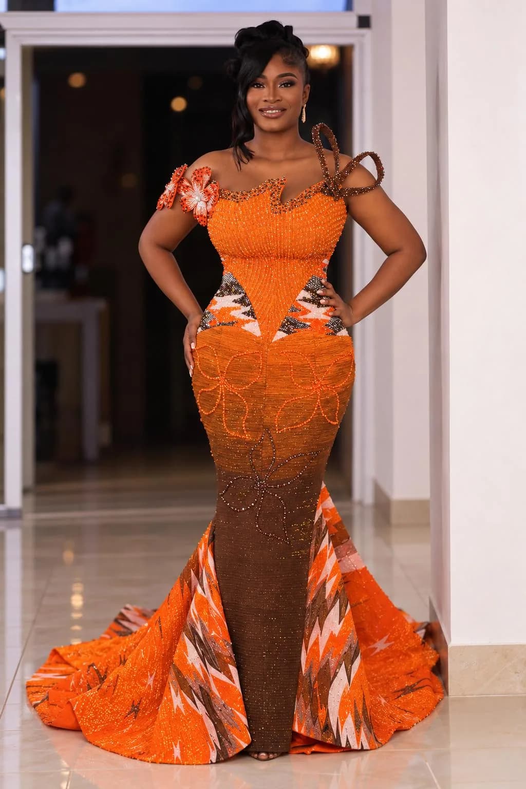 Client wearing a bespoke Magmens Couture amber beaded lace gown with off-shoulder floral appliqué, a ruffled peplum waist and a Kente-print train sweeping the floor.